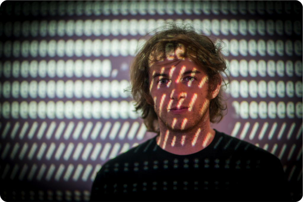 Portrait of Dmitri Cherniak with rows of projected light marks across his face and the wall behind