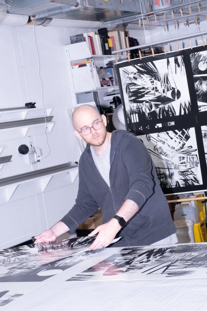 Dmitri Cherniak sorting large black and white Light Years prints on a table in a print studio